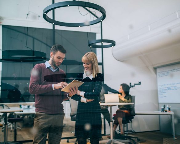 Two coworkers standing in an office, holding a digital tablet